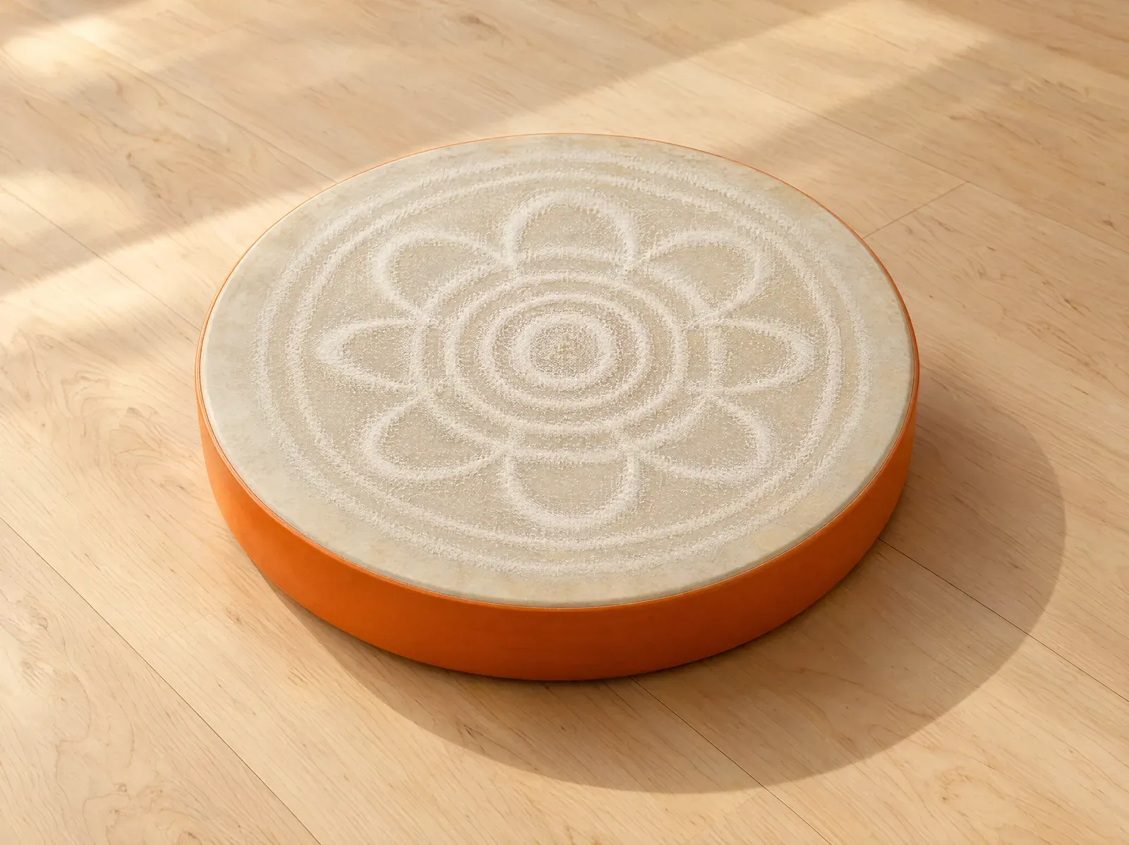 A frame drum with a tangerine rim; fine sand on its skin has settled into a pattern of rings and petals.